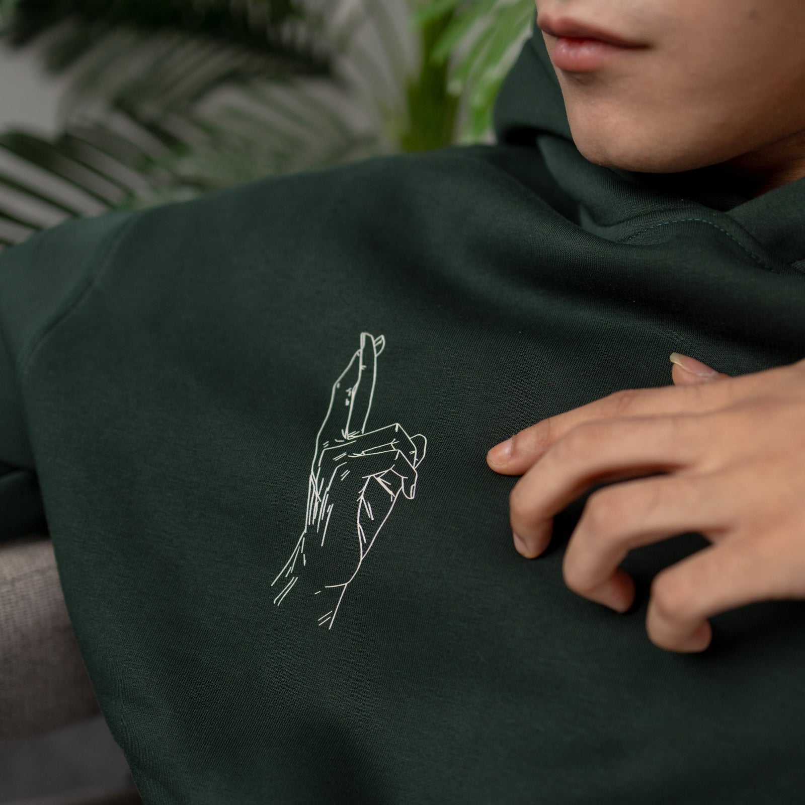 Person wearing a dark green hoodie with a white line drawing of a hand on the chest.