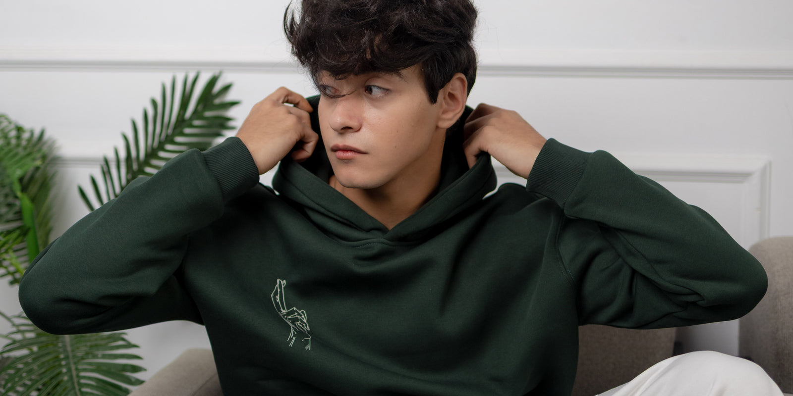 Person wearing a green hoodie with a logo, sitting indoors.