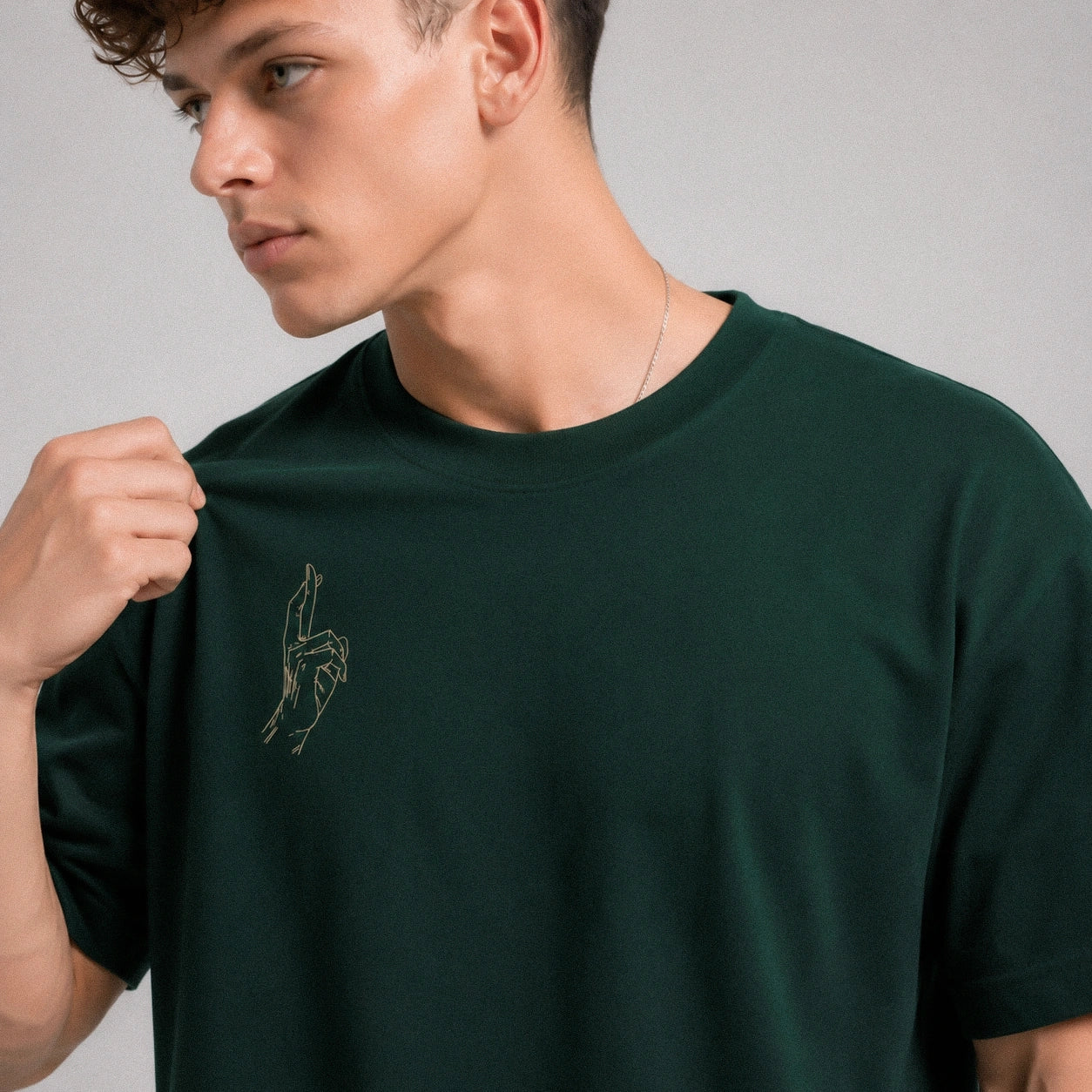 Man wearing a dark green t-shirt with a small graphic on a plain background