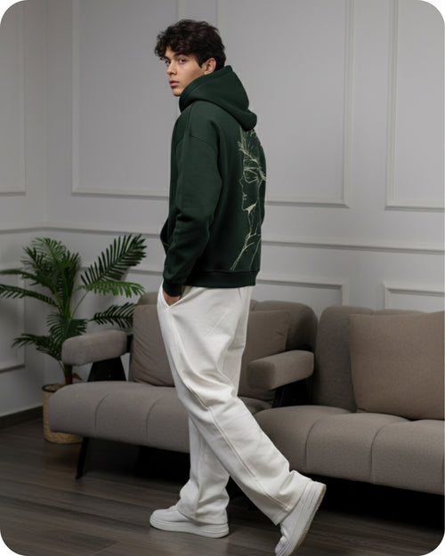 Person wearing a green hoodie and white pants in a living room setting