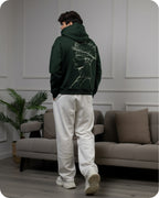 Person wearing a dark green hoodie with a graphic design in a living room setting