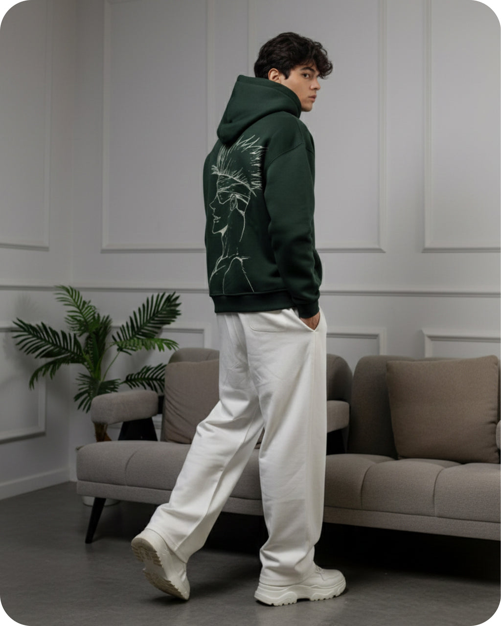 Person wearing a green hoodie with a graphic design, standing in a modern living room.