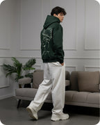 Person wearing a green hoodie with a graphic design, standing in a modern living room.