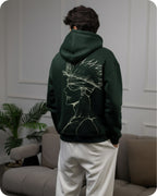 Person wearing a dark green hoodie with a white graphic design in a living room setting.