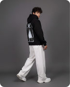 Person wearing a black hoodie with a graphic design on the back, white pants, and white shoes against a gray background
