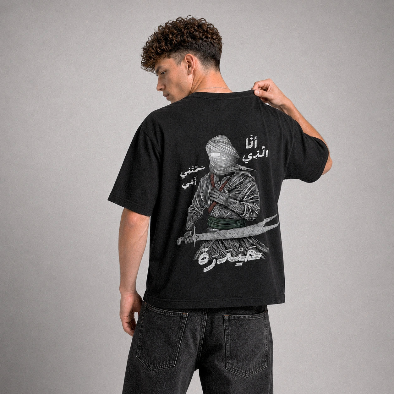 Person wearing a black t-shirt with a graphic design on the back against a gray background