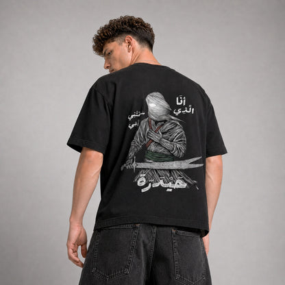 Person wearing a black t-shirt with a graphic design and text on the back, standing against a gray background.