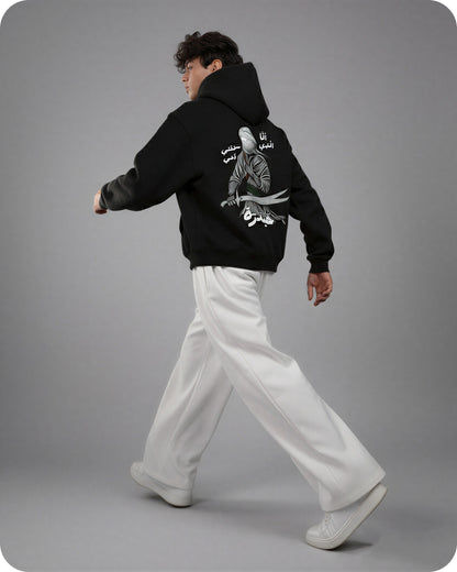 Person wearing a black hoodie with white text and graphics on the back, walking against a gray background