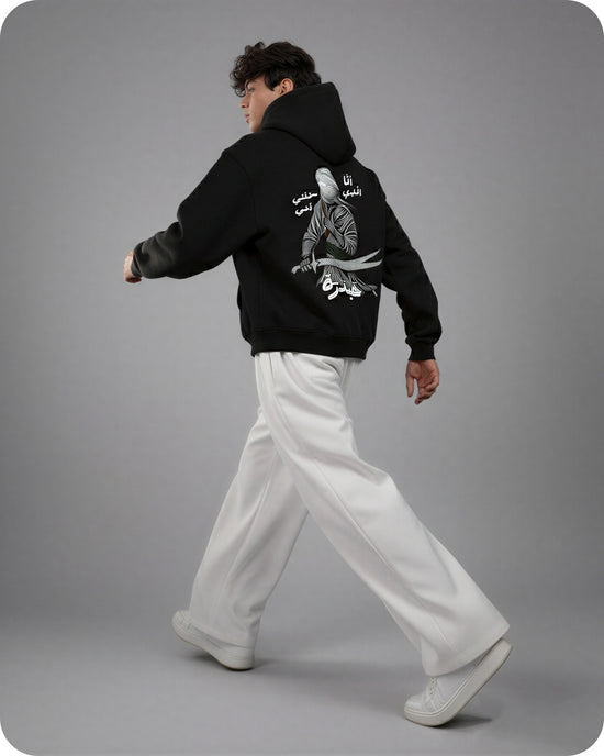 Person wearing a black hoodie with white text and graphics on the back, walking against a gray background