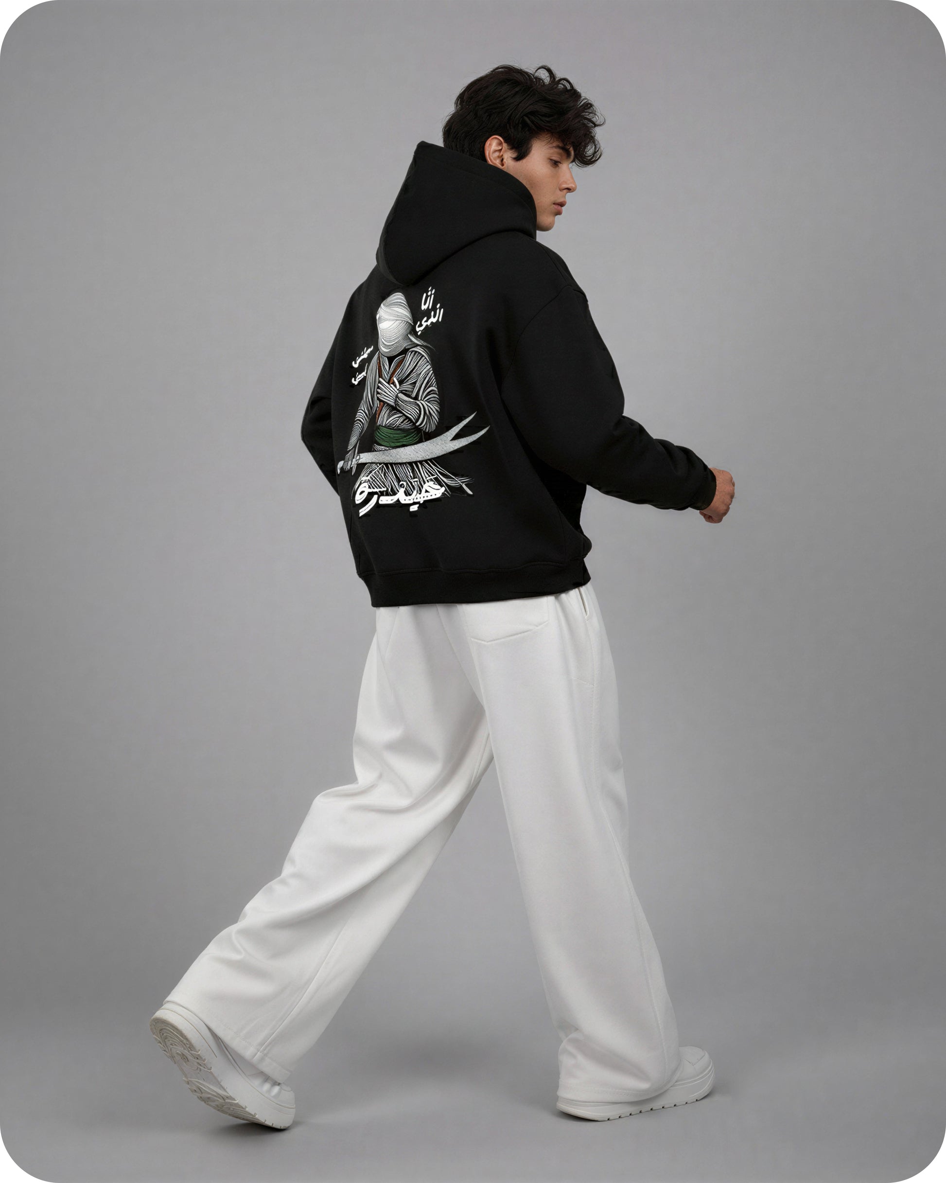 Person wearing a black hoodie with a graphic design on the back, standing against a gray background