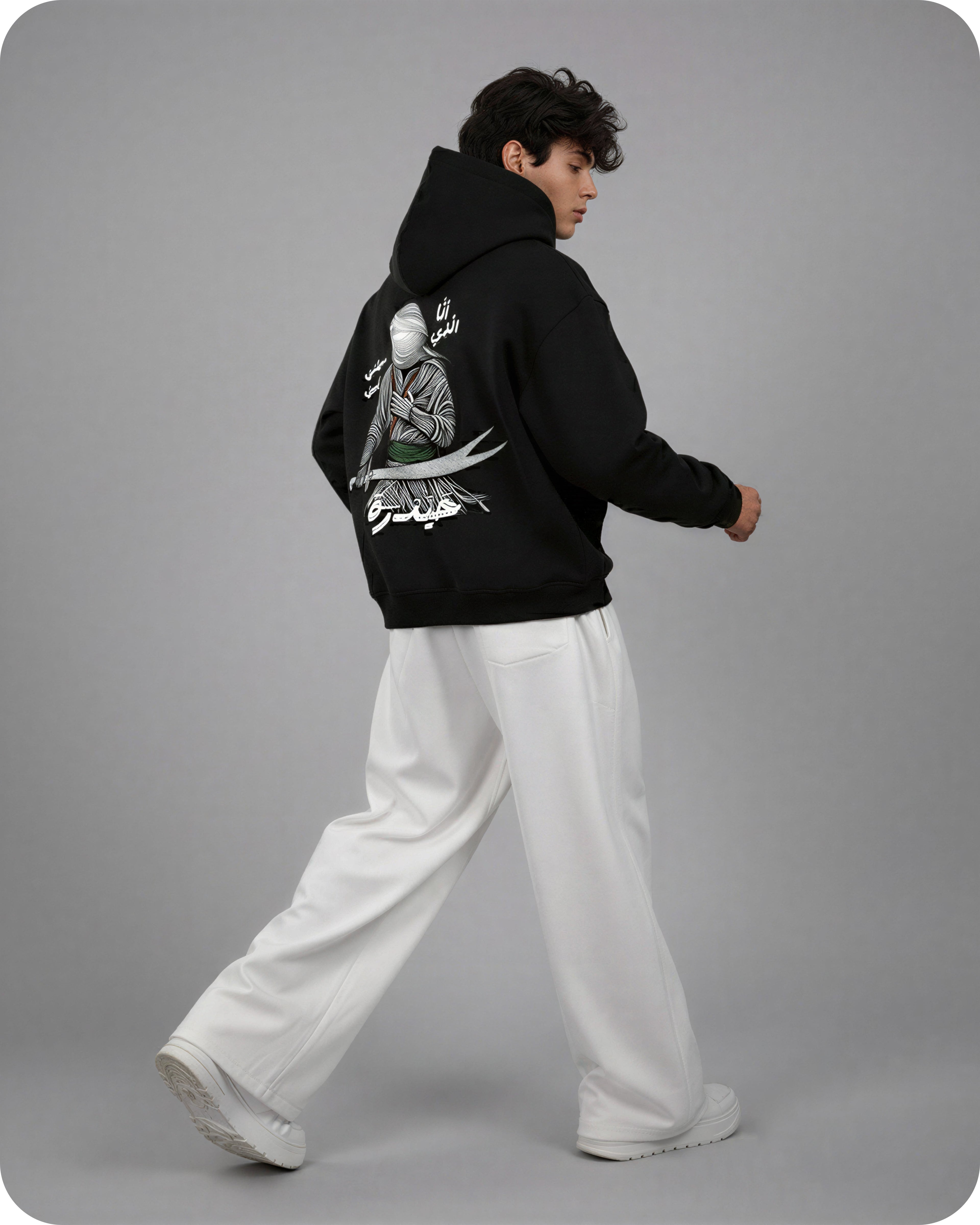 Person wearing a black hoodie with a graphic design on the back, standing against a gray background