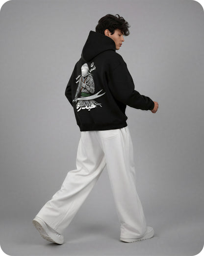 Person wearing a black hoodie with a graphic design on the back, standing against a gray background