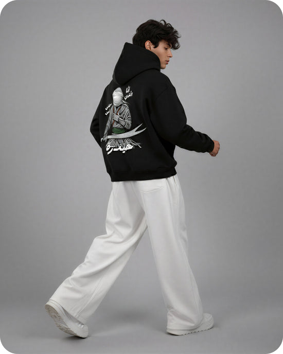 Person wearing a black hoodie with a graphic design on the back, standing against a gray background