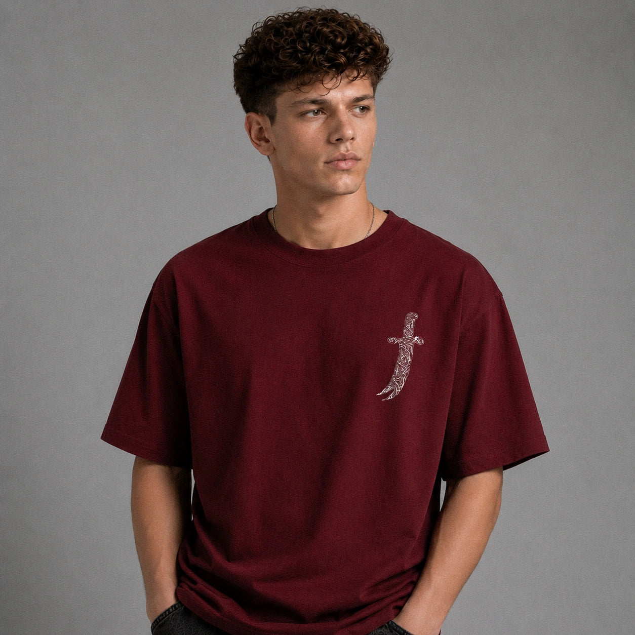 A man wearing a maroon t-shirt with a large graphic print of a bandit and Arabic text, shown from the back against a gray studio background.