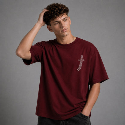 A man wearing a maroon short-sleeve t-shirt with a large graphic print on the back, shown from behind against a neutral gray background.