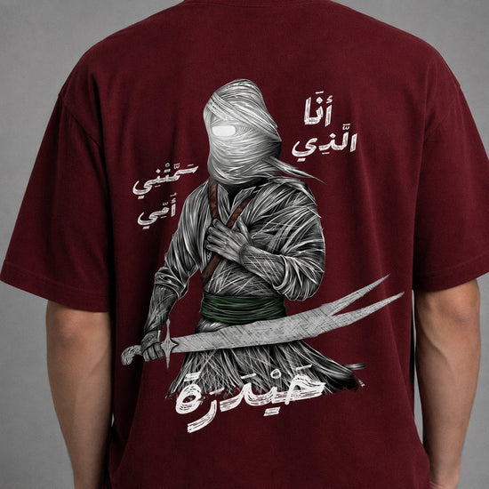 A young man modeling a short-sleeve crewneck t-shirt in deep burgundy. The shirt features a textured, metallic silver dagger graphic printed on the left chest.