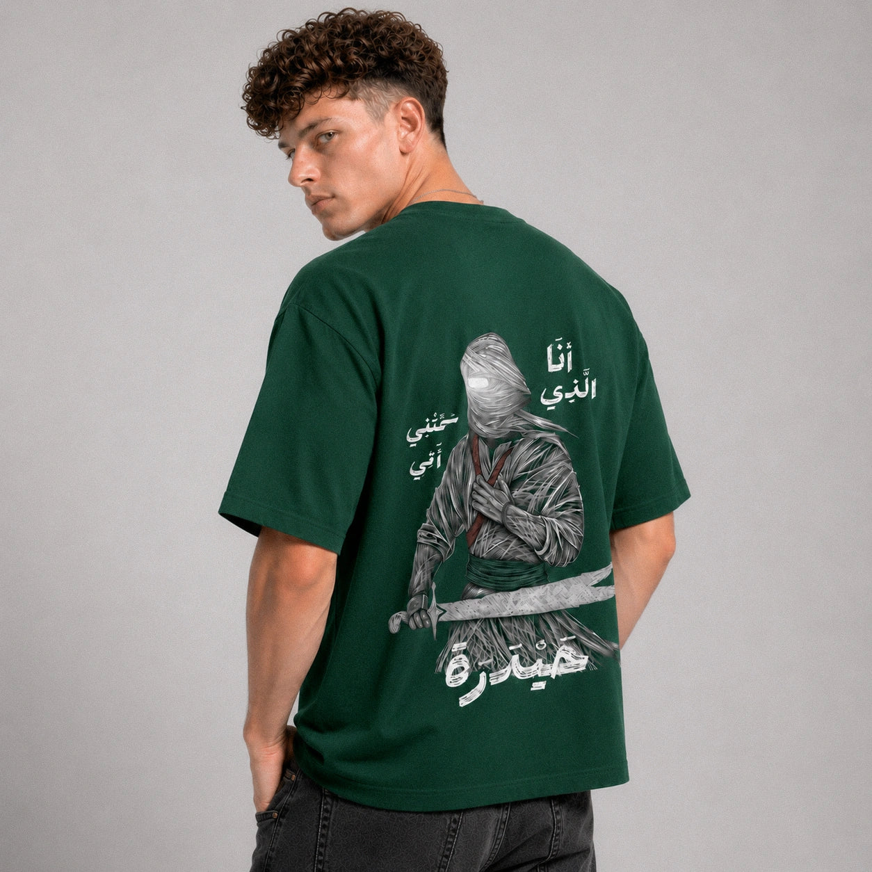 Person wearing a green t-shirt with a graphic and text on the back, standing against a gray background
