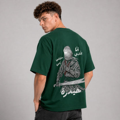 Person wearing a green t-shirt with a graphic and text on the back, standing against a gray background
