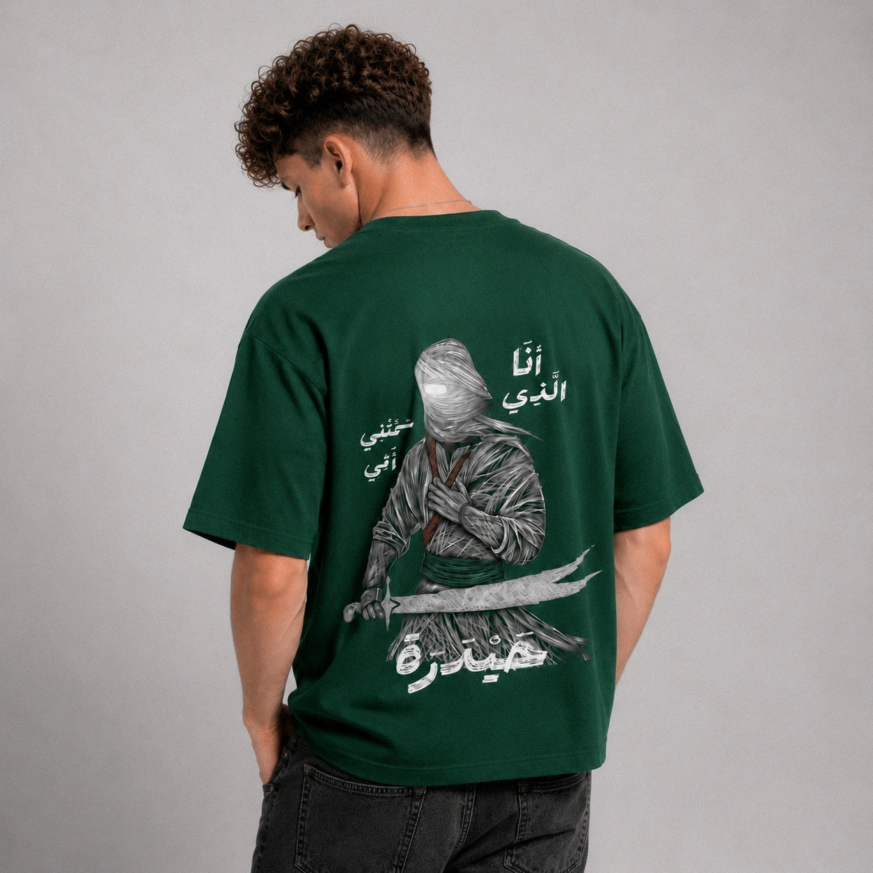 Person wearing a green t-shirt with a graphic design on the back, standing against a gray background