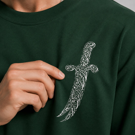 Person wearing a dark green sweatshirt with a white dagger design, pointing to the design with their finger.