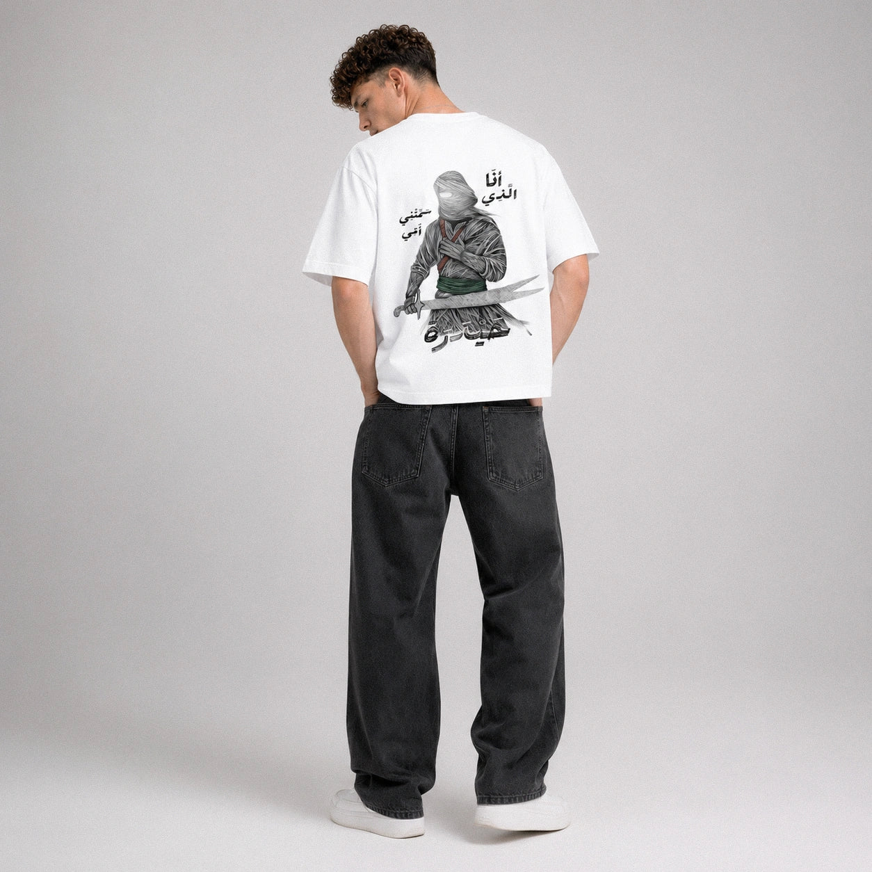 Person wearing a white t-shirt with a graphic design on the back, standing against a plain background.