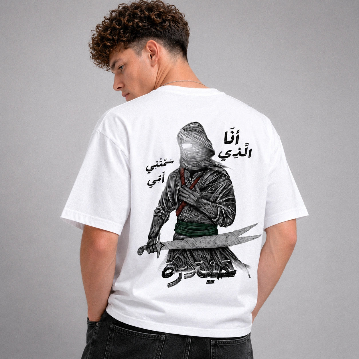 Person wearing a white t-shirt with a graphic design and text on the back, standing against a gray background.