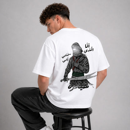 Person wearing a white t-shirt with a graphic design and text on the back, sitting on a stool against a gray background.