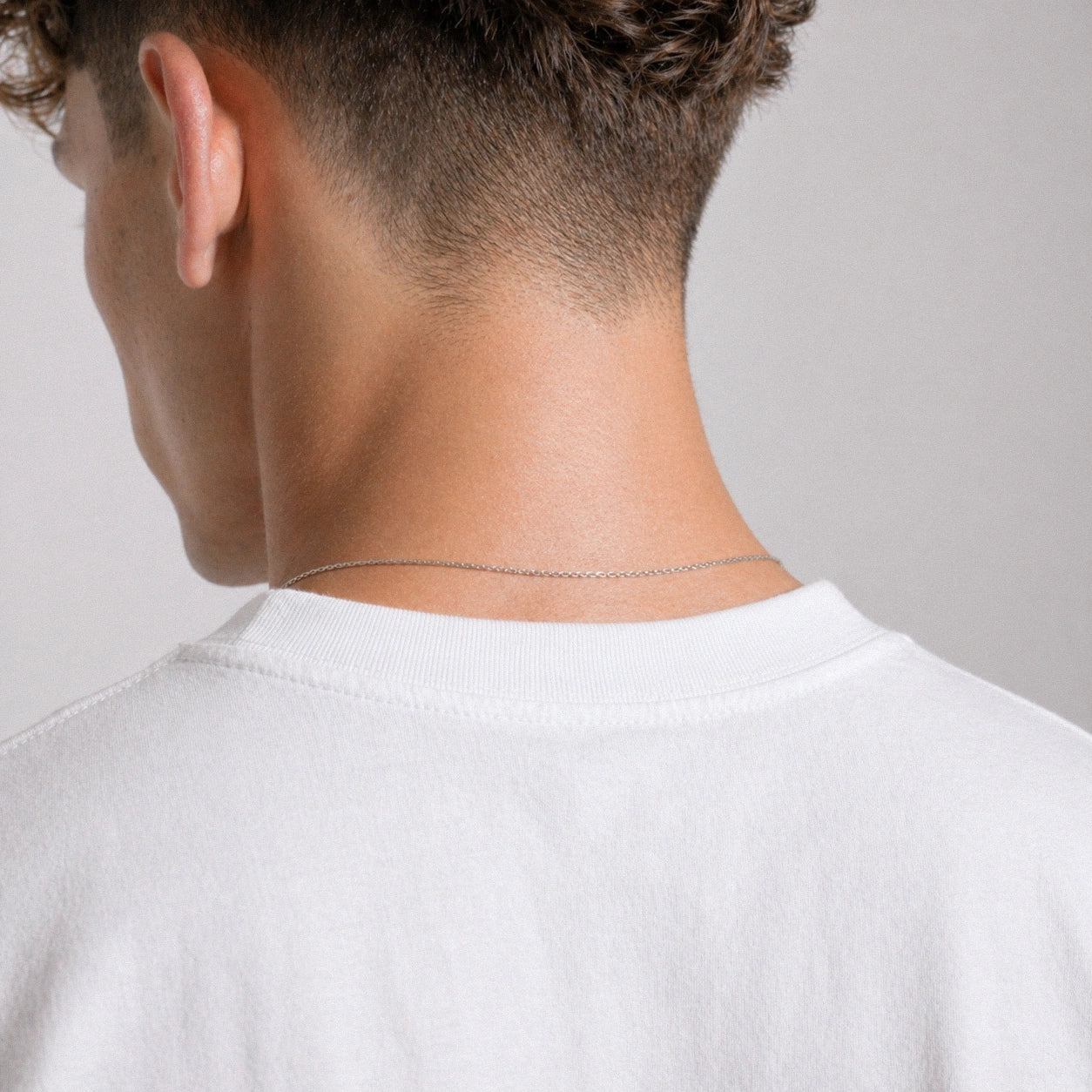 Person wearing a thin silver chain necklace on a plain background