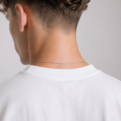 Person wearing a thin silver chain necklace on a plain background