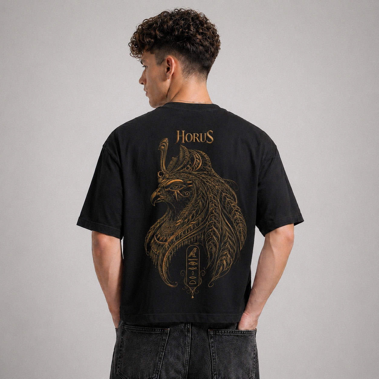 Person wearing a black t-shirt with gold 'Horus' design on the back against a gray background