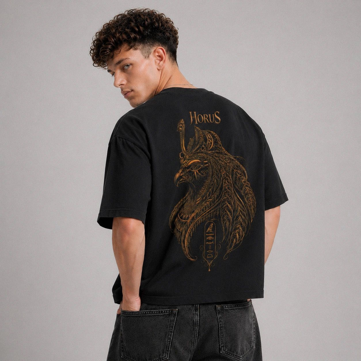 Person wearing a black t-shirt with a gold graphic design on the back, set against a gray background