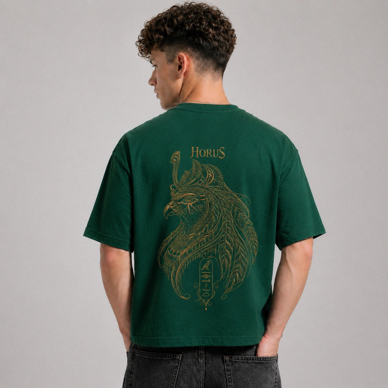 Person wearing a green t-shirt with a gold graphic and 'Horus' text on the back, against a gray background