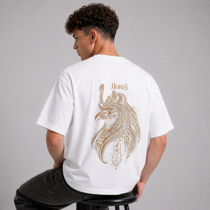 Person wearing a white t-shirt with a Horus design on the back, sitting on a stool against a gray background.
