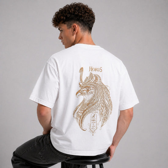 Person wearing a white t-shirt with a Horus design on the back, sitting on a stool against a gray background.