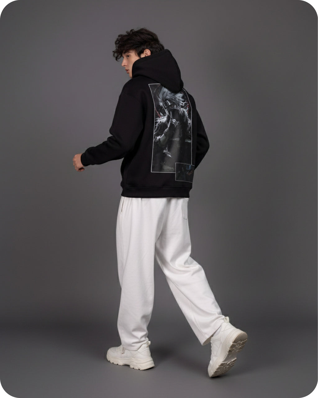 Person wearing a black hoodie with a graphic design on the back, white pants, and white shoes against a gray background