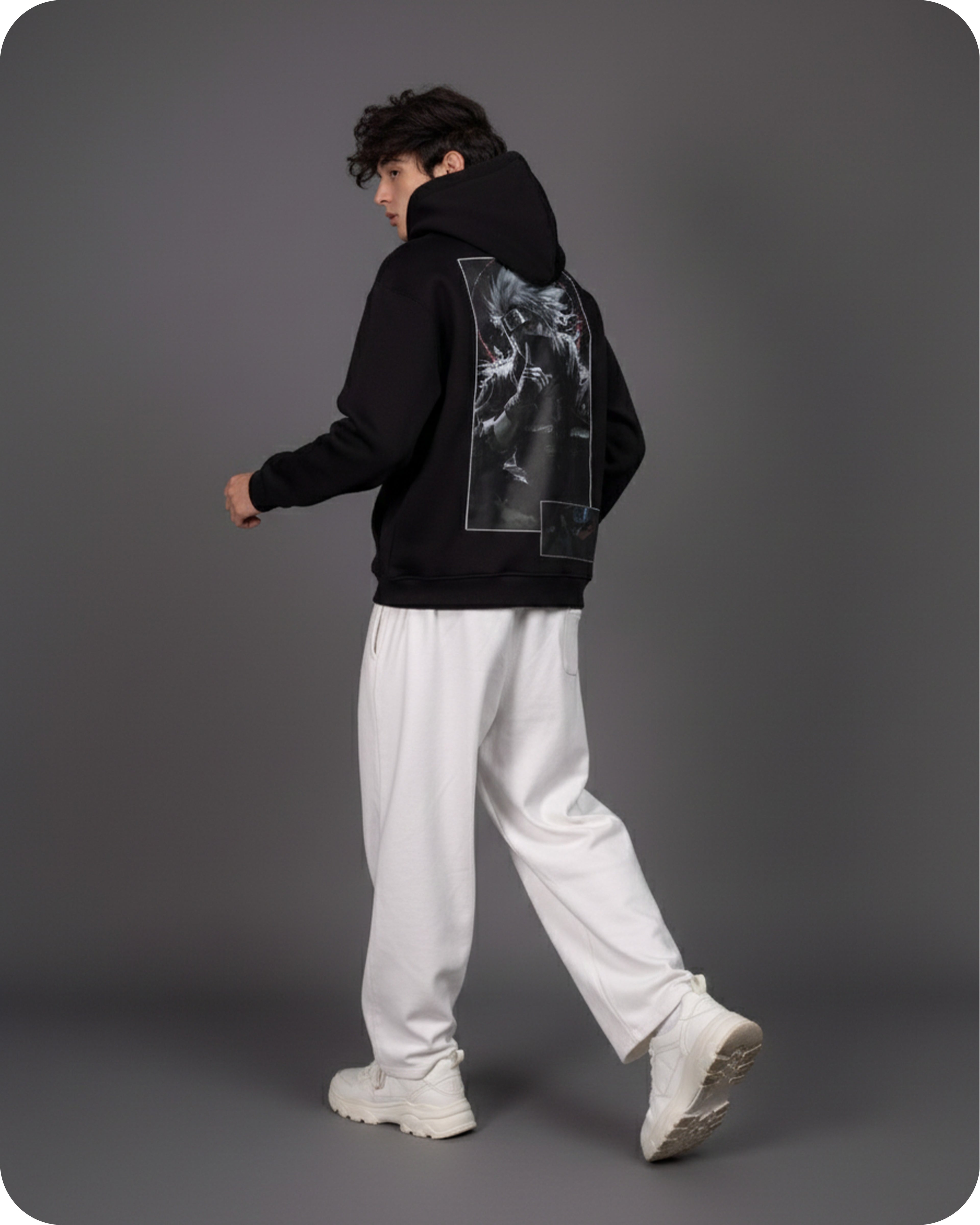 Person wearing a black hoodie with a graphic design on the back, white pants, and white shoes against a gray background