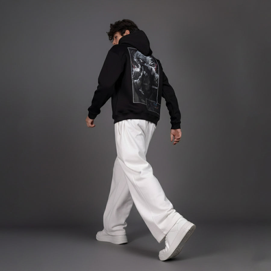 Person wearing a black hoodie with a graphic design on the back, white pants, and white shoes against a gray background