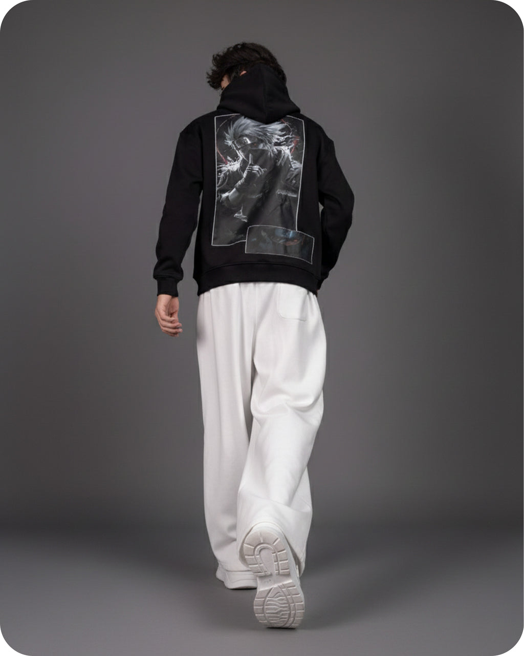 Person wearing a black hoodie with a graphic design on the back, standing against a gray background