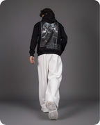 Person wearing a black hoodie with a graphic design on the back, standing against a gray background