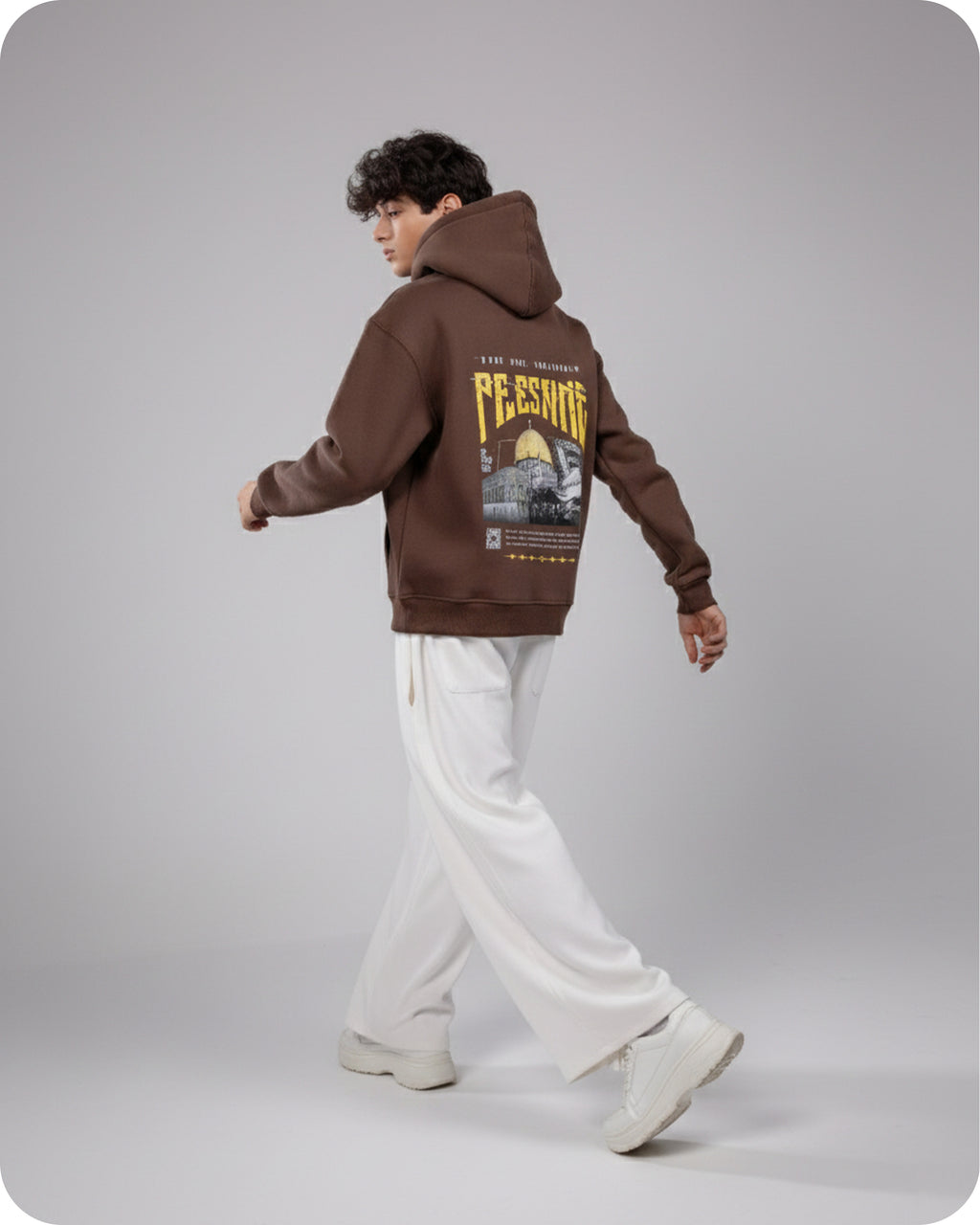 Person wearing a brown hoodie with graphic design on the back, standing against a plain background