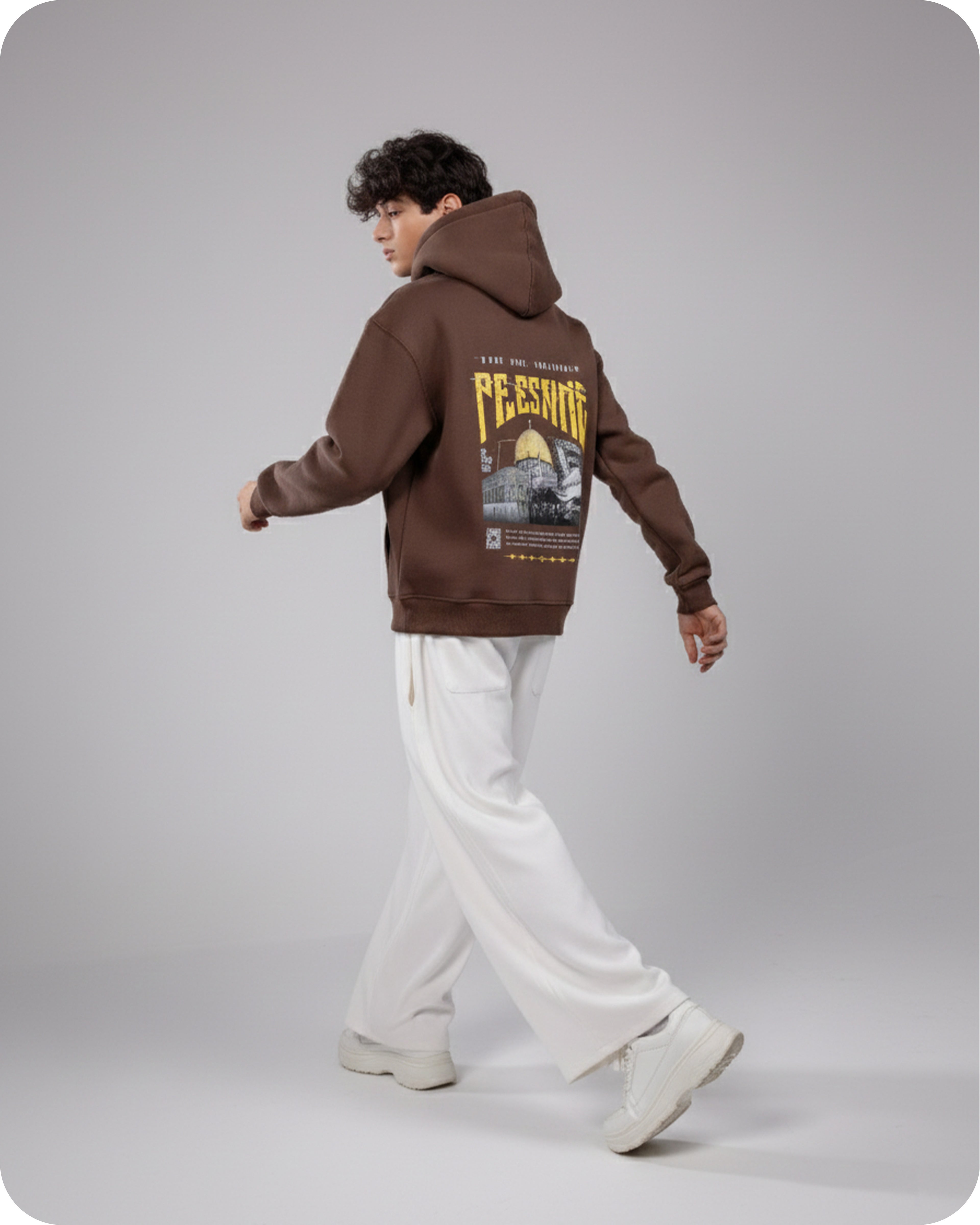 Person wearing a brown hoodie with graphic design on the back, standing against a plain background