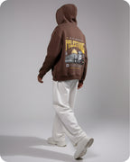 Person wearing a brown hoodie with graphic design on the back against a gray background