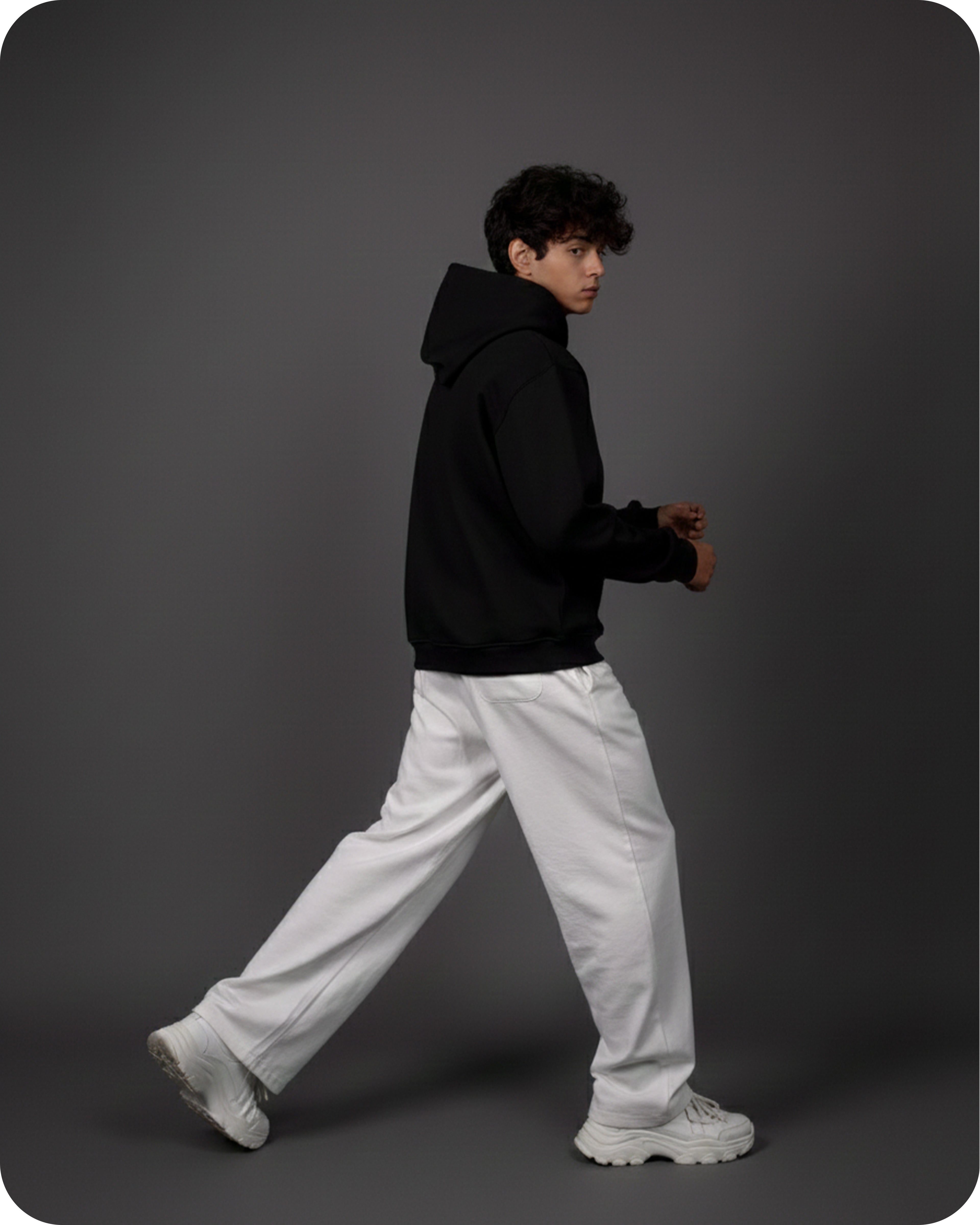 Person wearing a black hoodie and white pants walking on a gray background