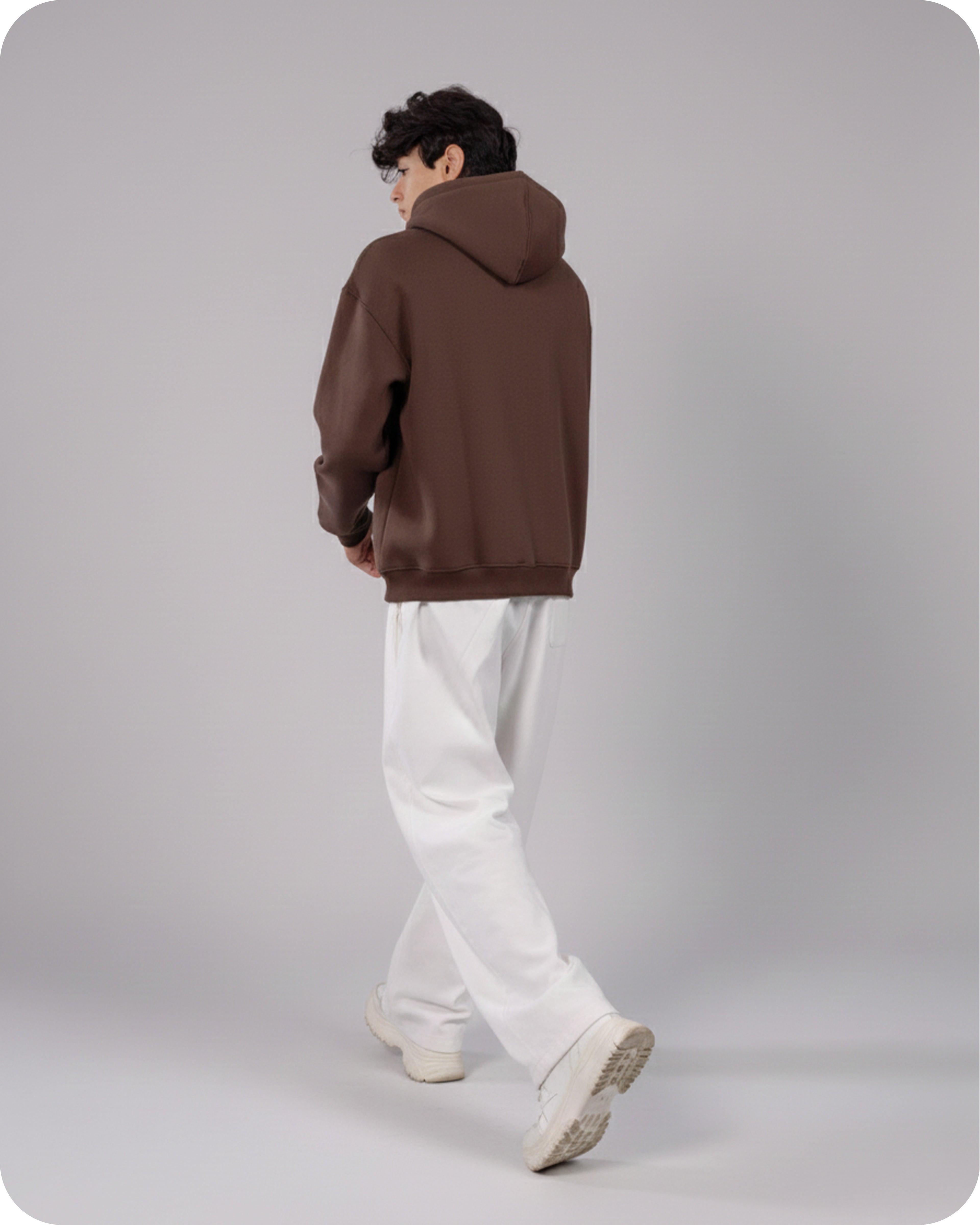 Person wearing a brown hoodie and white pants on a gray background