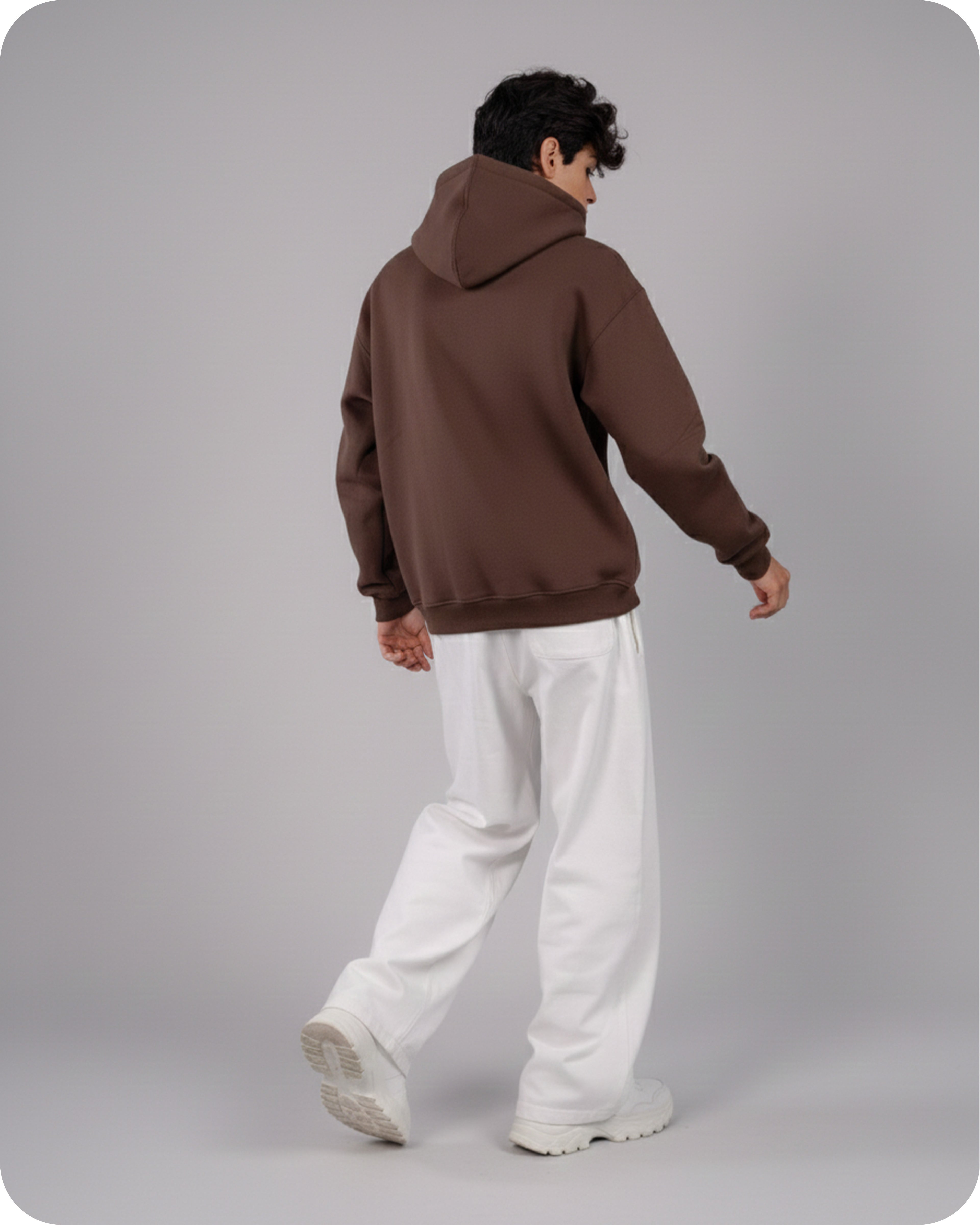 Person wearing a brown hoodie and white pants on a gray background