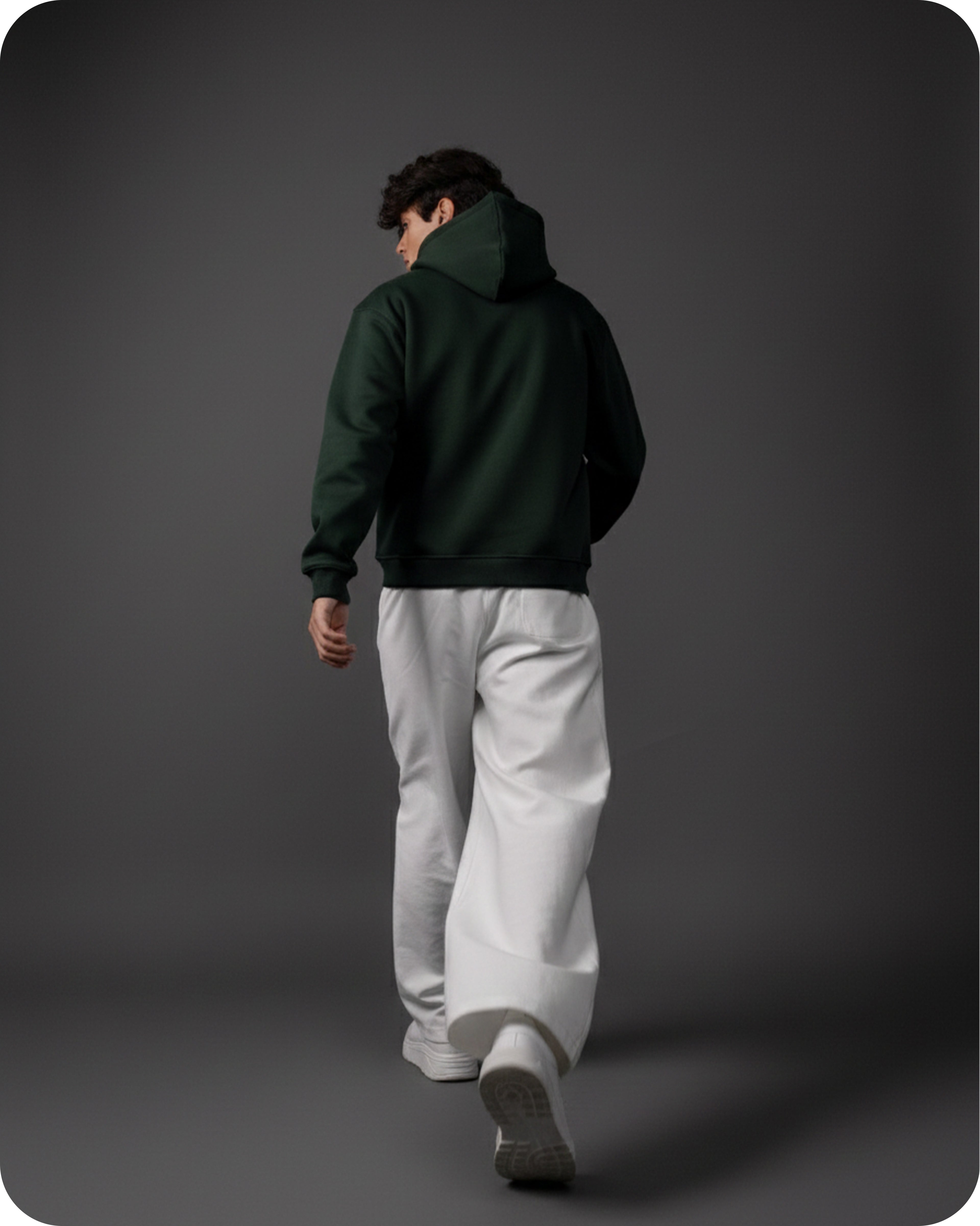 Person wearing a dark green hoodie and light gray pants walking on a dark background