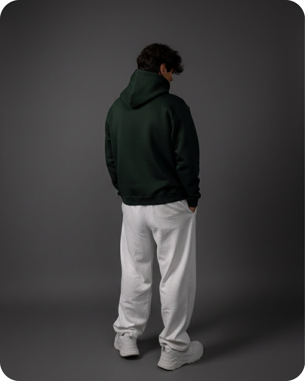 Person wearing a dark green hoodie and white pants on a gray background