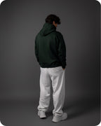Person wearing a dark green hoodie and white pants on a gray background