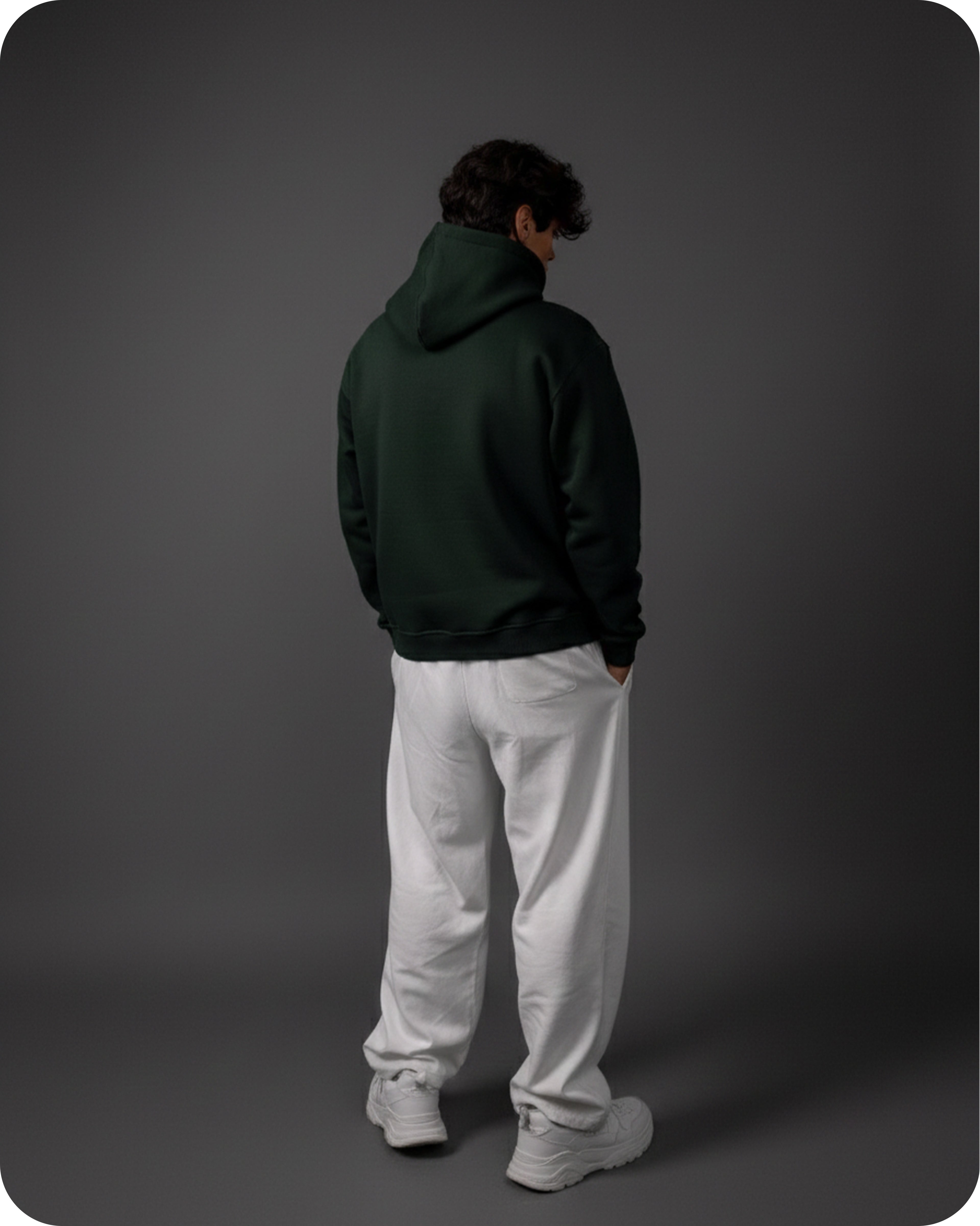 Person wearing a dark green hoodie and white pants on a gray background