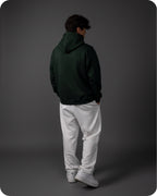 Person wearing a dark green hoodie and white pants on a gray background